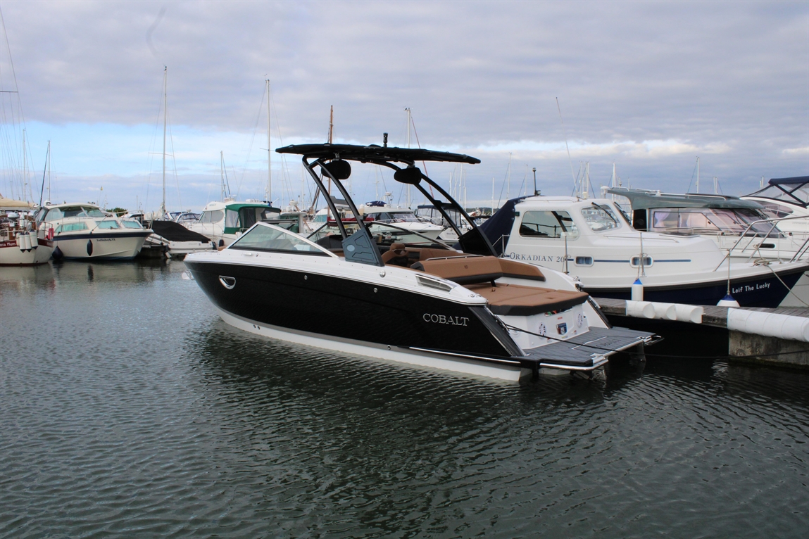 A Cobalt boat docked in a marina, surrounded by other boats, with a cloudy sky reflecting on the water.